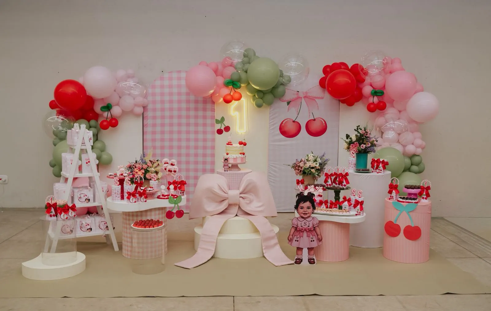 Decoração com tema cereja, com painéis xadrez rosa, laço rosa grande e balões vermelhos, rosa e verdes