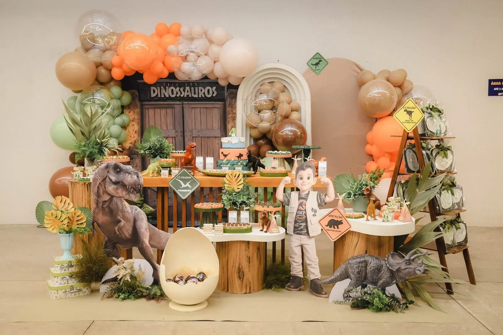 Decoração com tema dinossauros, com portão de madeira, dinossauros e balões em laranja, verde e bege