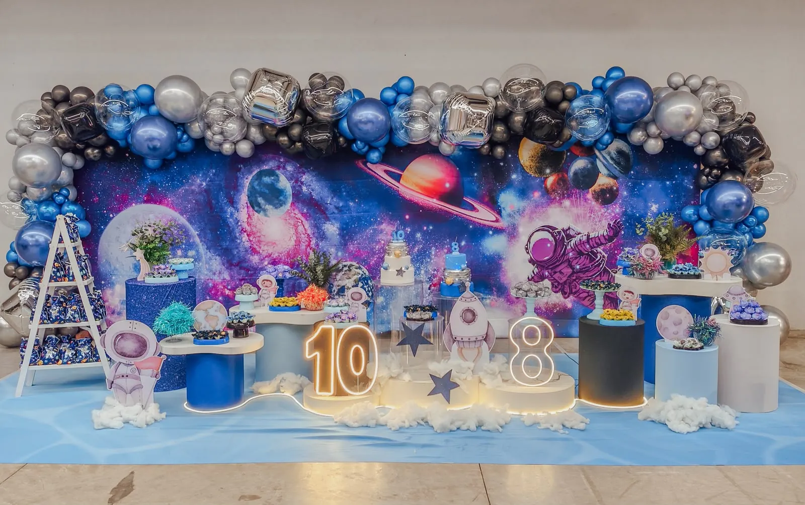 Decoração com tema galáxia, com painel de planetas e arco de balões em azul, prata e preto